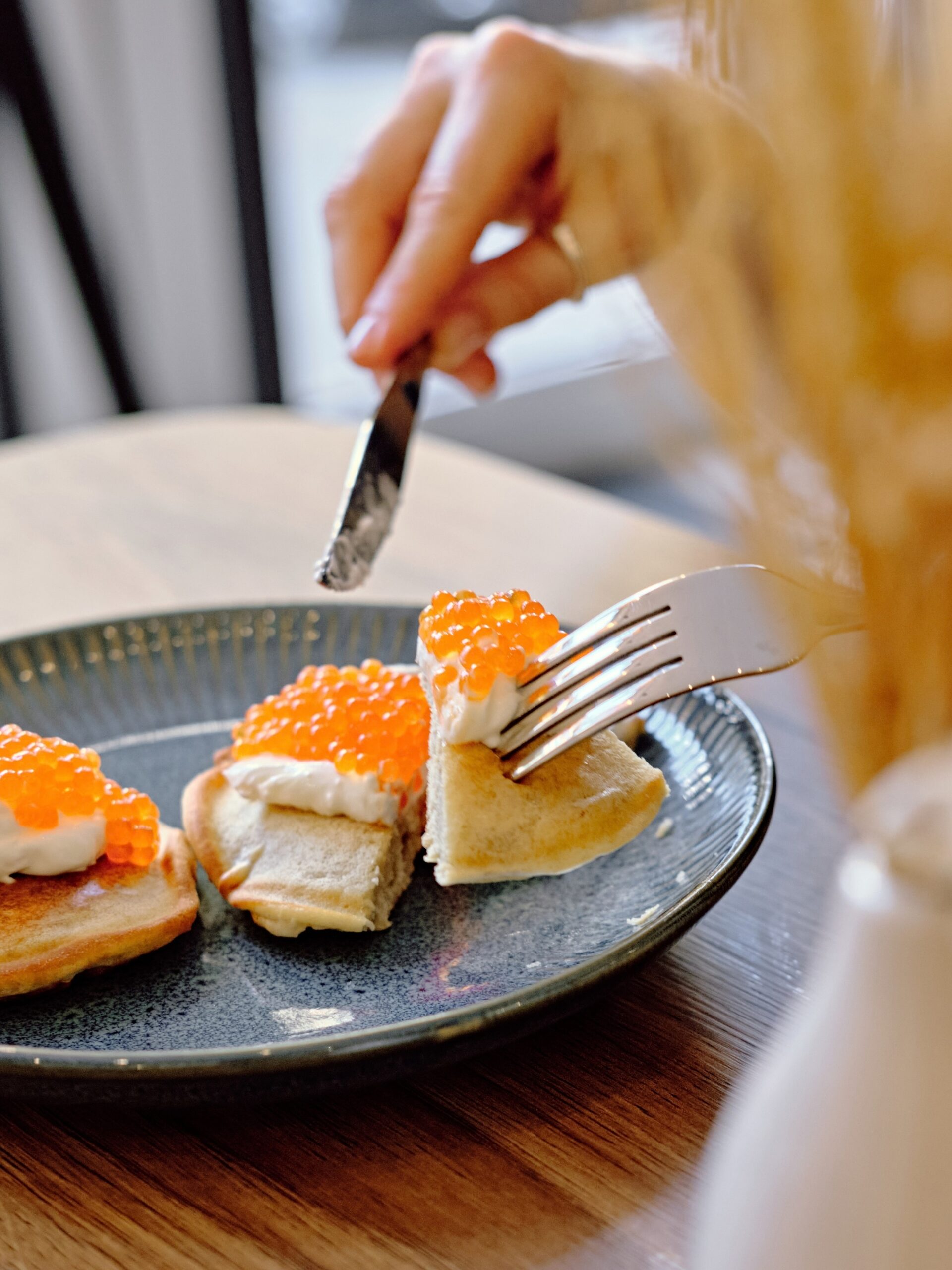 Hands cutting into homemade pancakes topped with red caviar and sour cream