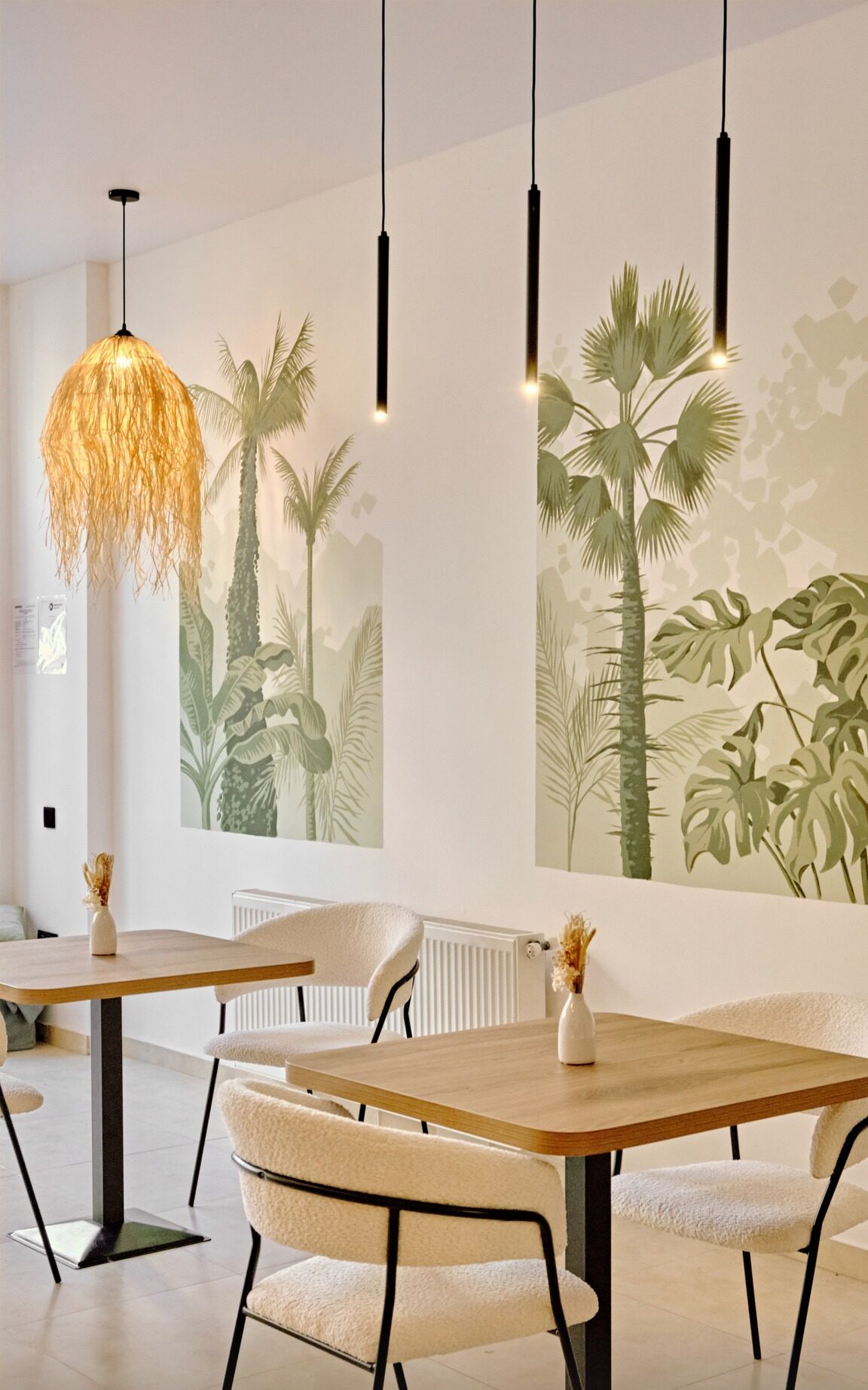 Unity Bistro dining room: wooden tables with cream chairs, a raffia pendant lamp and a jungle mural of palms and monstera on the wall