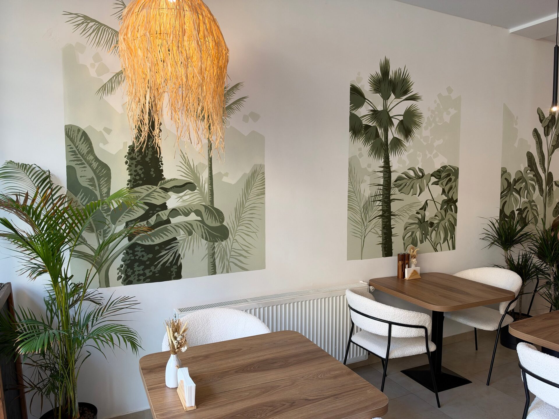 Jungle mural with palms and monstera above wooden tables and cream chairs