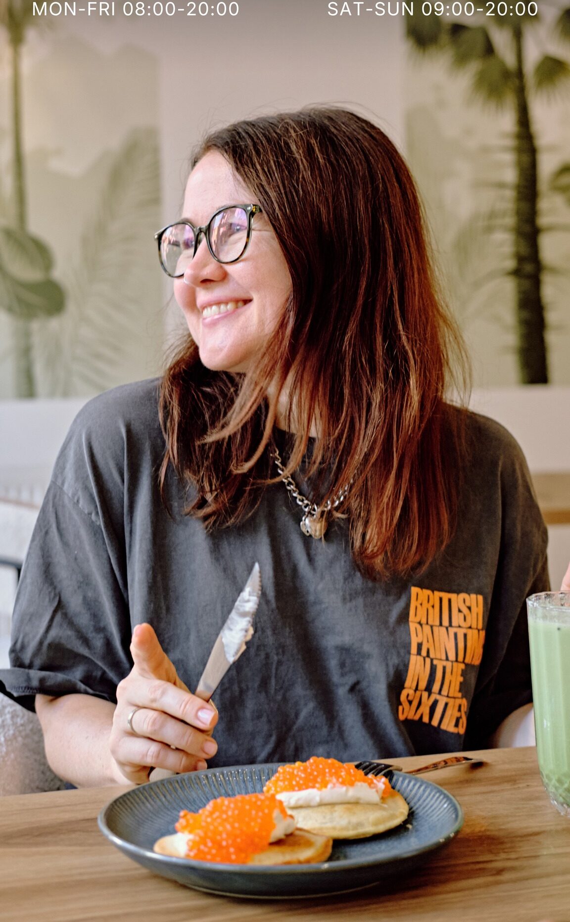 A guest at a table with pancakes, red caviar and a matcha drink, the mural behind her